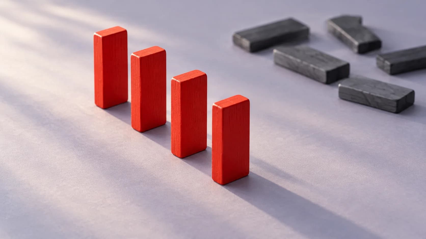 Illustrative still life of four upright red wooden blocks in a short sequence, with separate gray blocks lying behind them